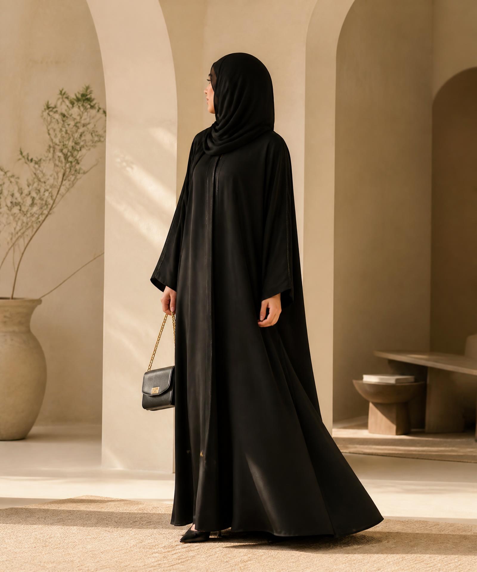 Woman wearing a flowing black Chann Taara abaya in a sunlit minimal interior